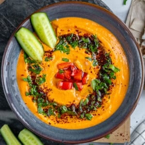Red pepper hummus topped with cucumber sticks, chopped parsley, chopped roasted red pepper and spices.