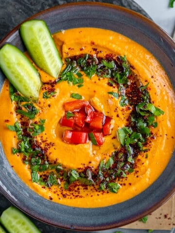 Red pepper hummus topped with cucumber sticks, chopped parsley, chopped roasted red pepper and spices.