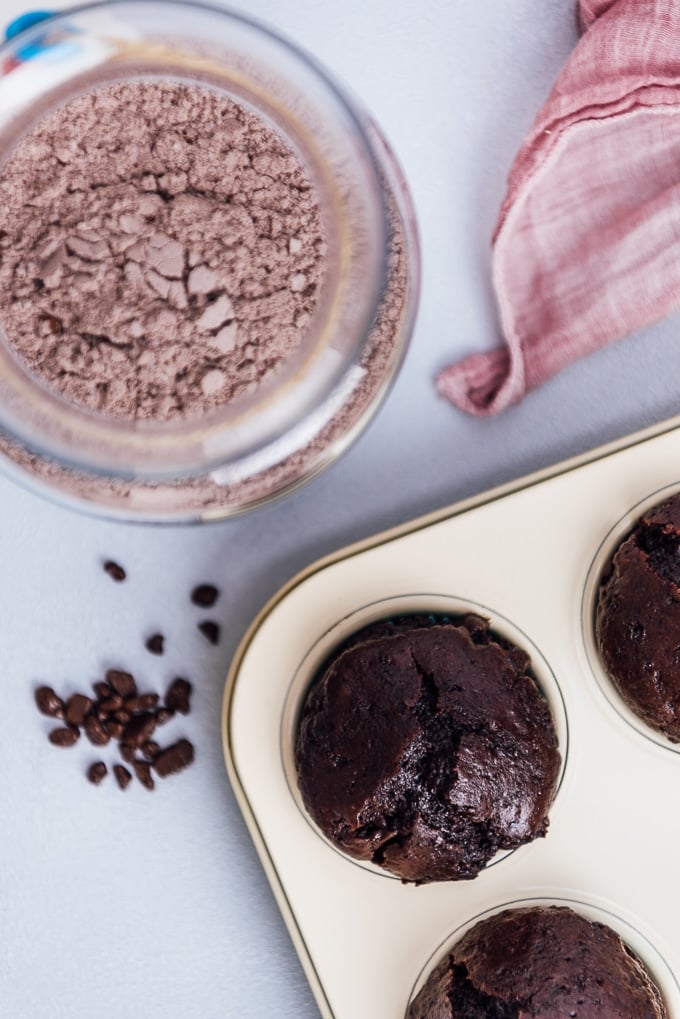 Chocolate cake mix in a jar and chocolate muffins in a muffin pan photographed from top view.