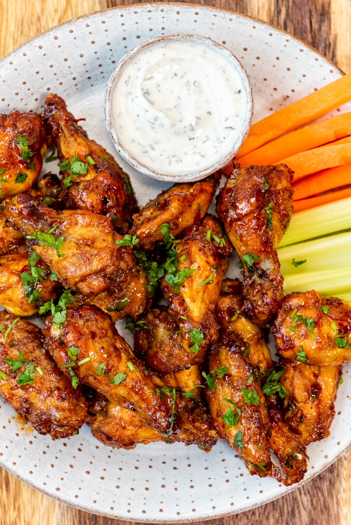 Baked buffalo wings served on a white plate with carrot and celery sticks and a yogurt dip sauce on the side.