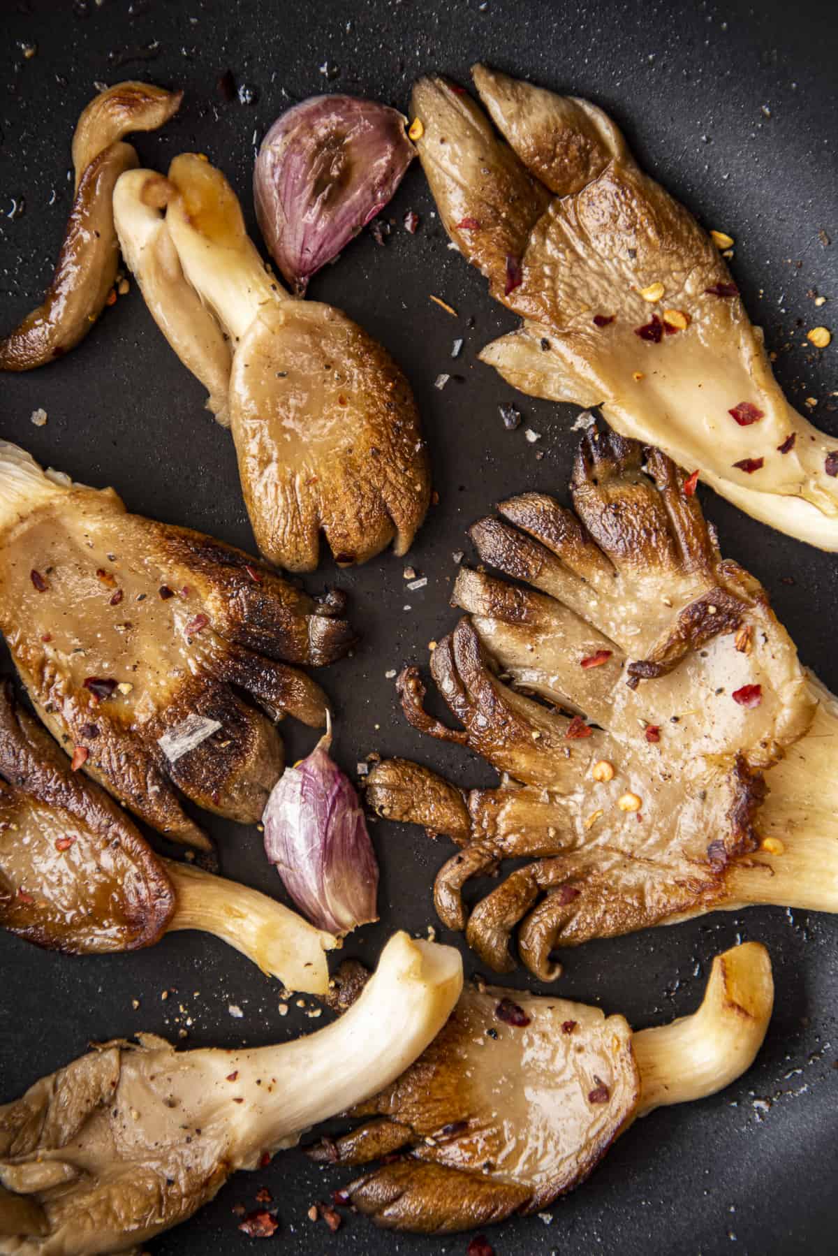 Cooked oyster mushrooms with garlic cloves in a non-stick pan.