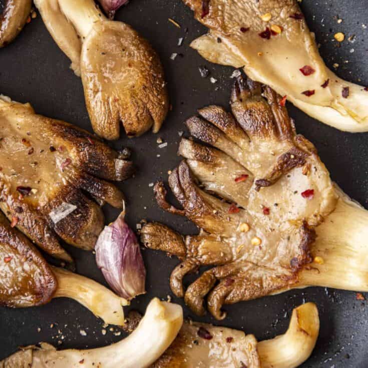 Oyster mushrooms cooked in a non-stick pan with garlic cloves until golden.
