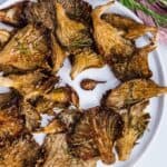 Roasted oyster mushrooms with rosemary served on a white plate.