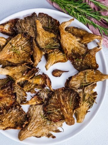 Roasted oyster mushrooms with rosemary served on a white plate.