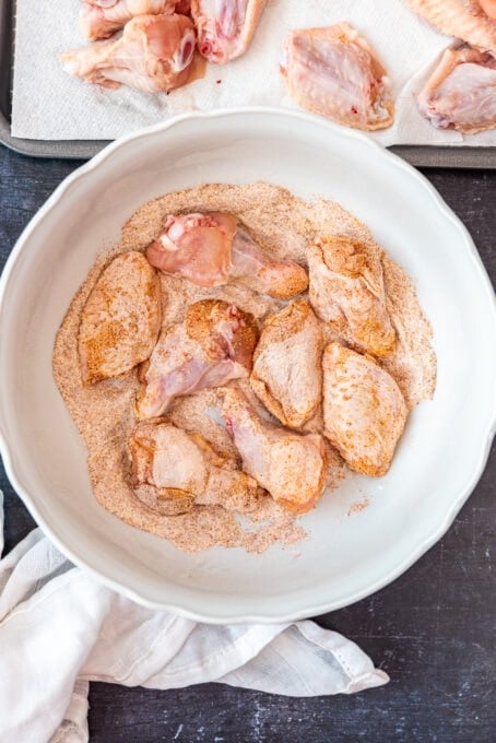 Chicken wings seasoned with spices and baking powder in a white bowl.