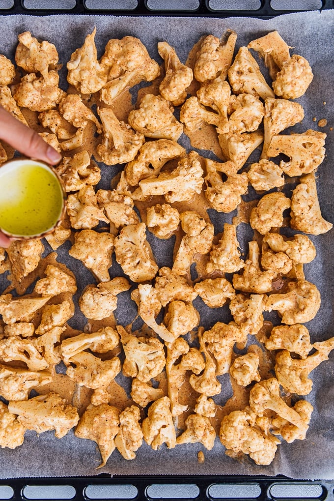 Drizzling olive oil over battered cauliflower florets on a baking sheet