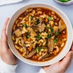 Woman holding a bowl of vegan oyster mushroom soup on a light background