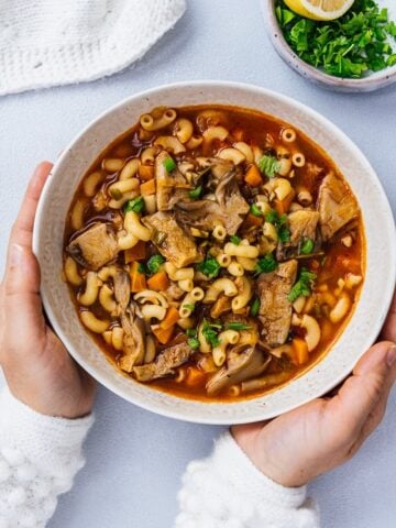 Woman holding a bowl of vegan oyster mushroom soup on a light background