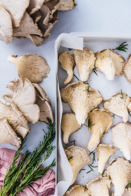 Oyster mushrooms with rosemary leaves on a baking sheet.