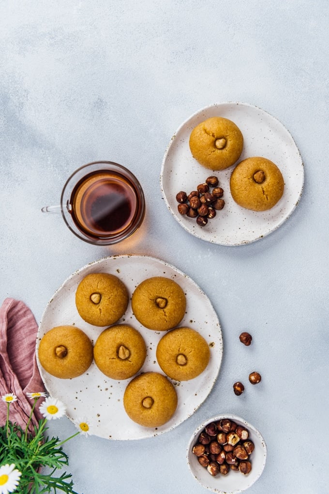 Semolina cookies soaked with sweet syrup on two ceramic plates accompanied by a cup of Turkish tea and hazelnuts