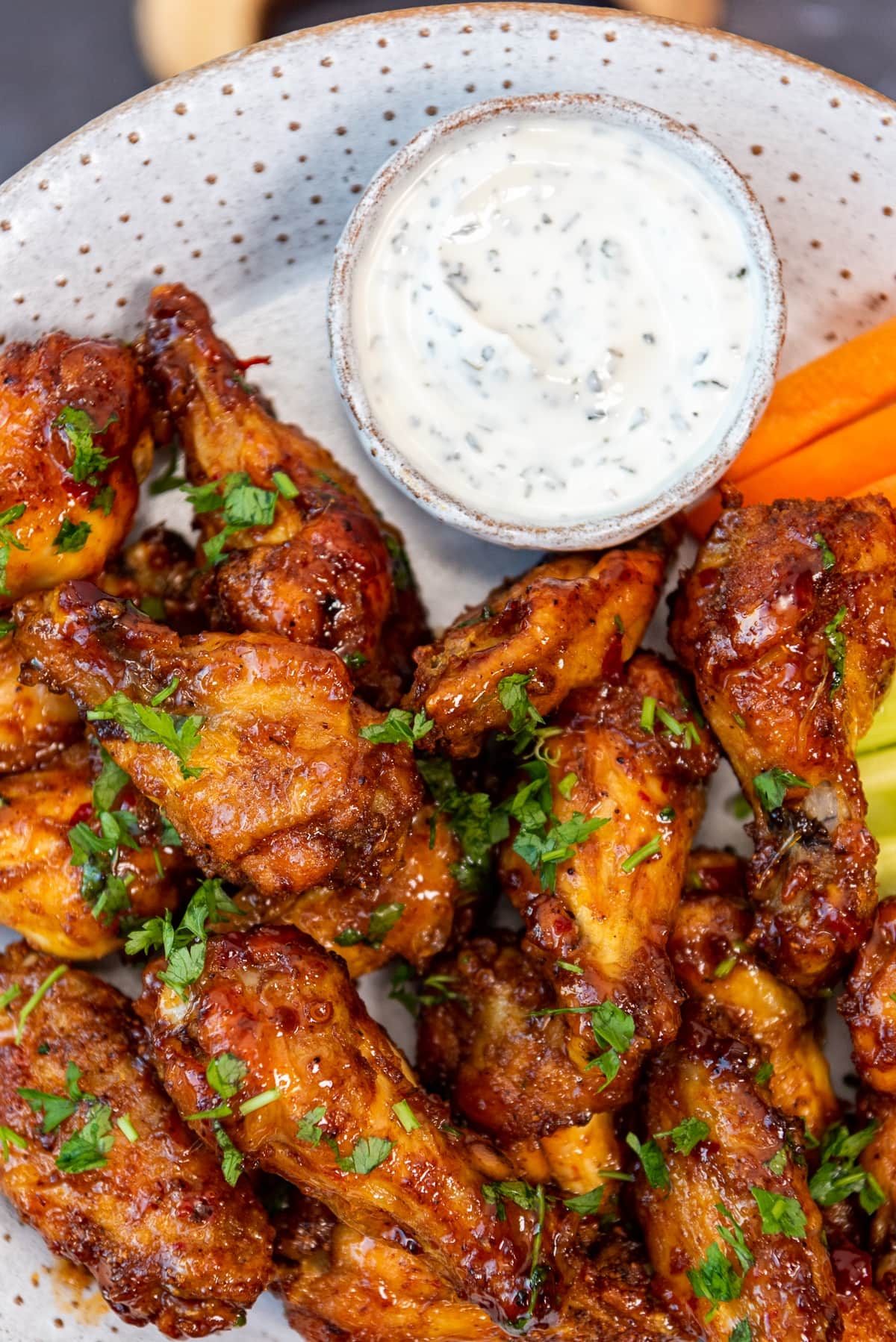 Spicy and crispy chicken wings served with a yogurt dip sauce, carrot and celery sticks on a white plate.