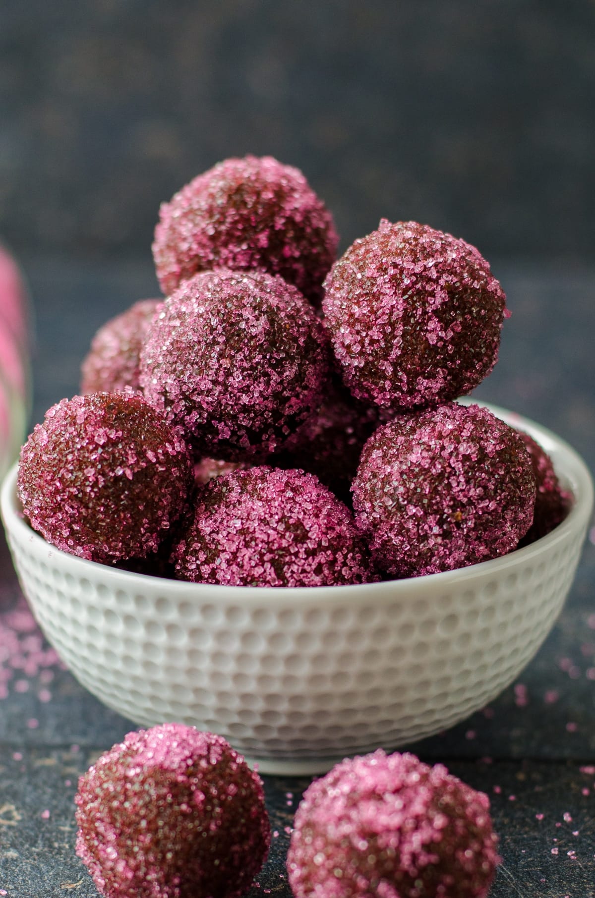 Chocolate truffles with biscuits coated with colored sugar in a white bowl on a dark background.