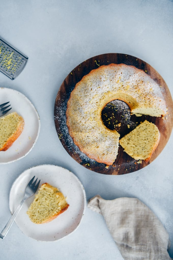 Moist lemon cake with poppy seeds on a wooden board and slices served on two plates