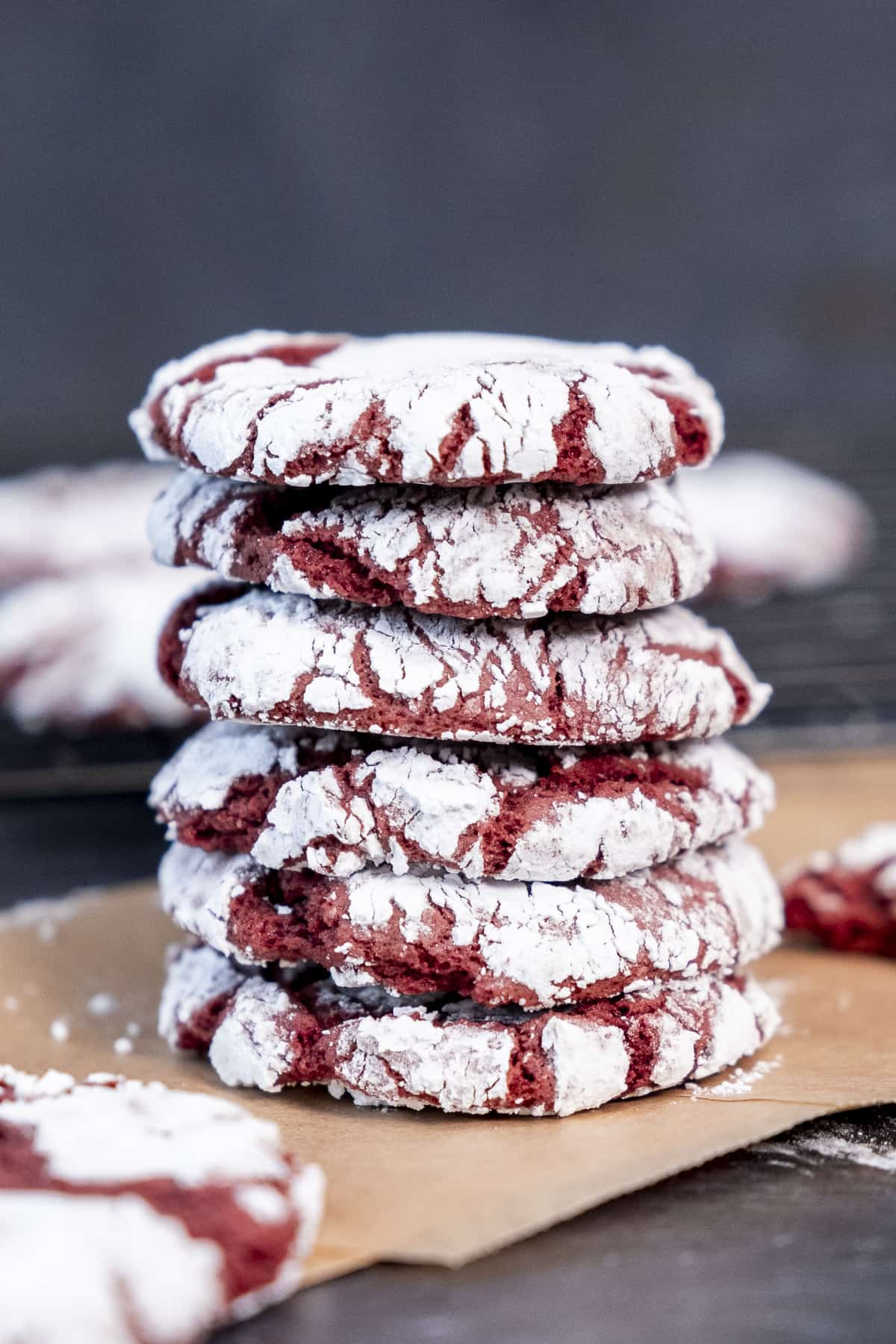 A stack of red velvet crinkle cookies coated with powdered sugar on a baking paper.