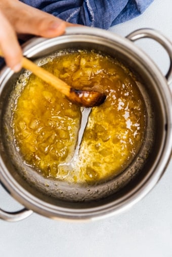 Hands stirring lemon jam with a wooden spoon in a pot.