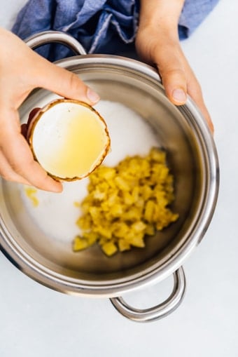 Woman pouring lemon juice in a pot with lemon zest to make lemon jam.