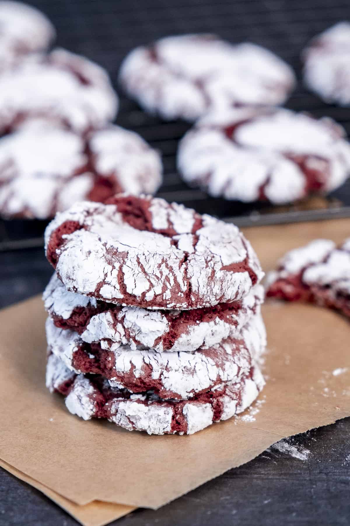 A stack of red velvet crinkle cookies on a baking paper, more cookies around them.