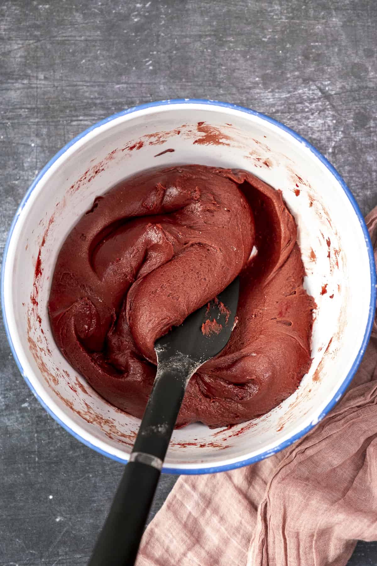 Red velvet cookie dough in a white bowl and a black spatula inside it.