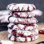 A stack of red velvet crinkle cookies on a baking paper with a dark background.