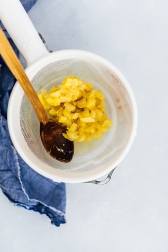 Cooked lemon slices and lemon zest on a strainer with a small wooden spoon.