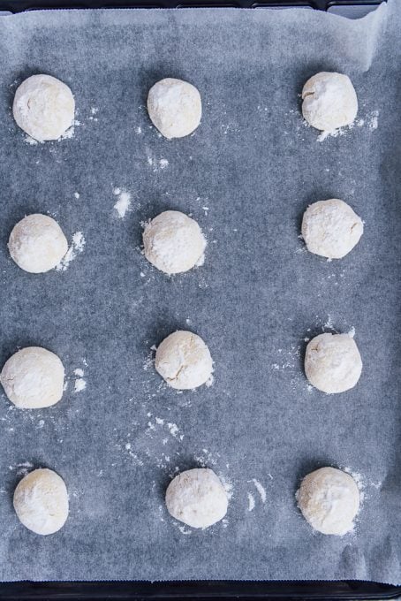 Lemon cookie balls coated with powdered sugar on a baking sheet.