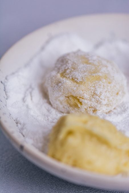 Lemon cookie balls in a bowl of powdered sugar.