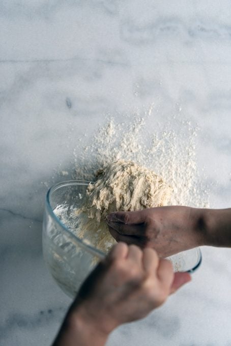 Transfering bread dough from a glass bowl onto a marble counter.