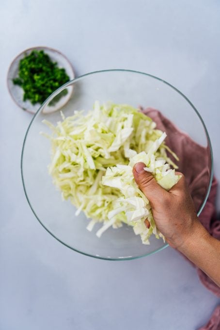 Hand scrunching shredded cabbage in a glass bowl.