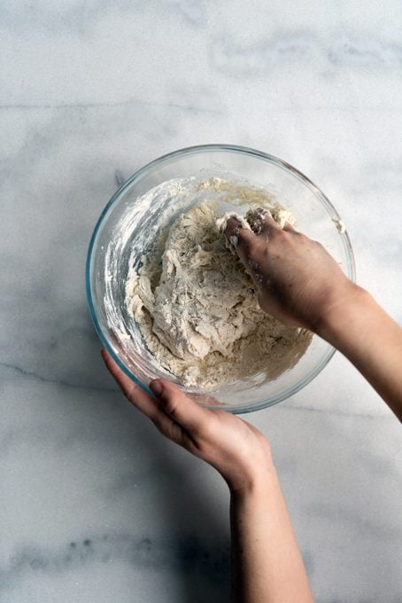 Mixing no yeast bread dough ingredients in a glass mixing bowl with a hand.