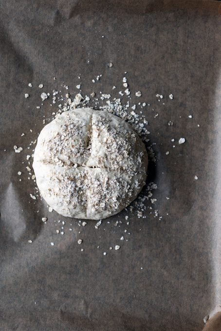 Homemade bread dough topped with oats on a baking sheet.