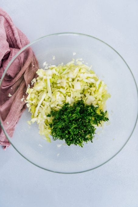 Shredded cabbage and chopped fresh dill in a glass bowl.
