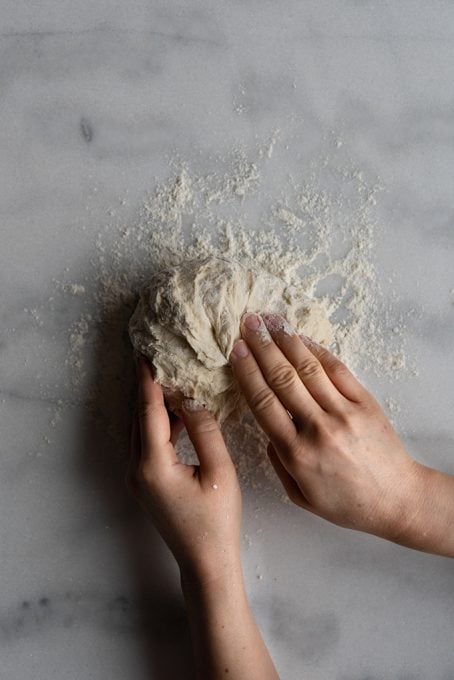 Hands shaping homemade bread dough into a ball.