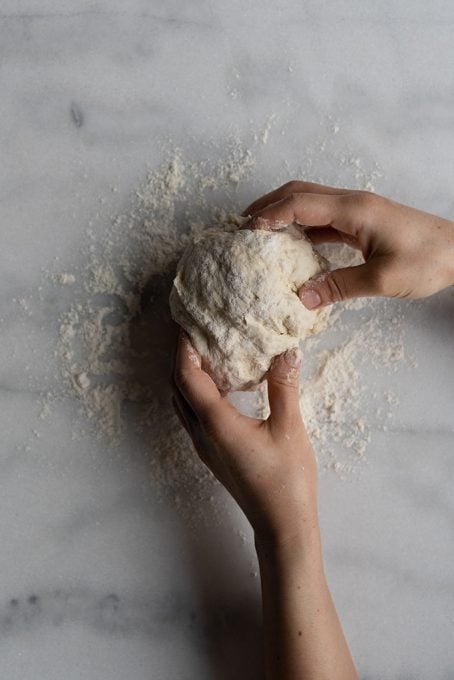 Hands shaping yeast free dough on a marble counter.