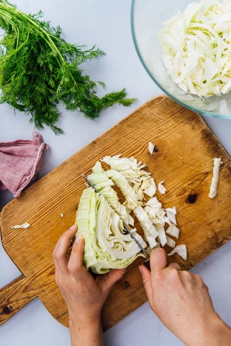 Hands chopping cabbage on a wooden cutting board.