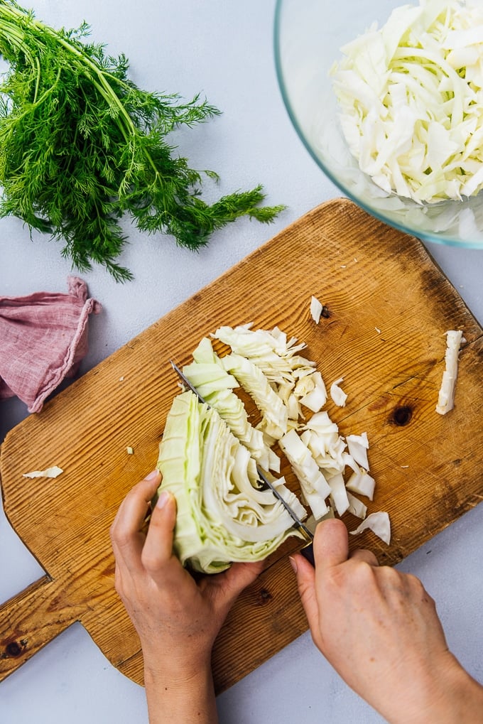 Hands chopping cabbage on a wooden cutting board.