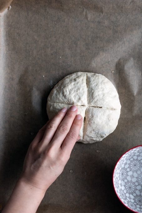 A hand wetting the top of a round bread dough.