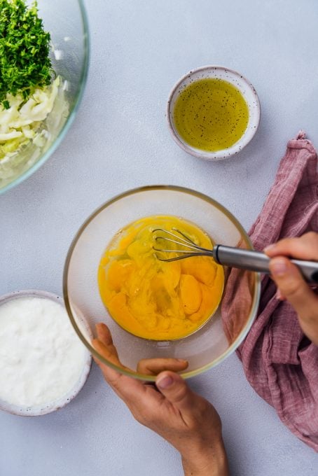 Hands whisking eggs in a glass bowl to make cabbage casserole.