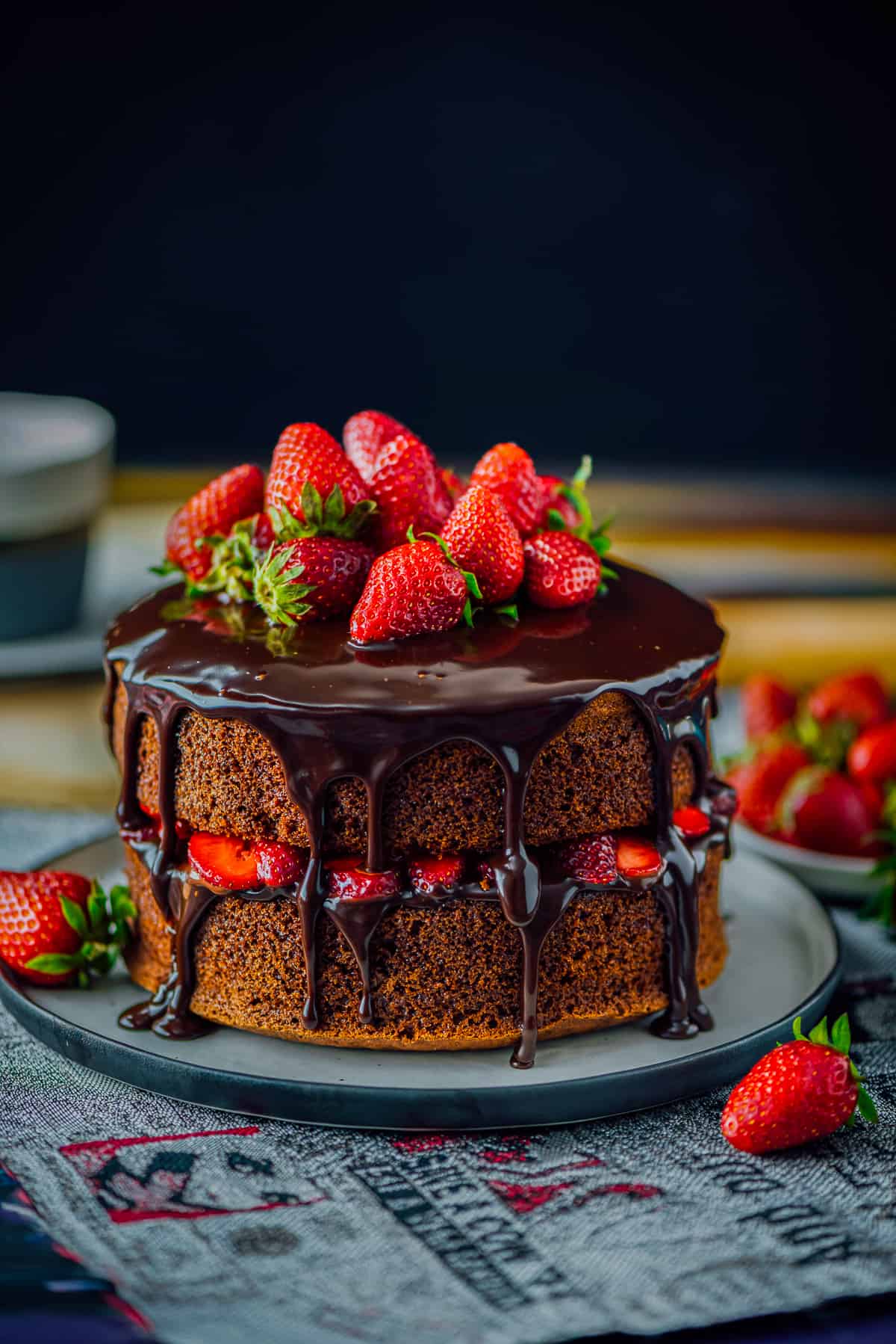 Chocolate cake with ganache and strawberries on a plate, strawberries around.