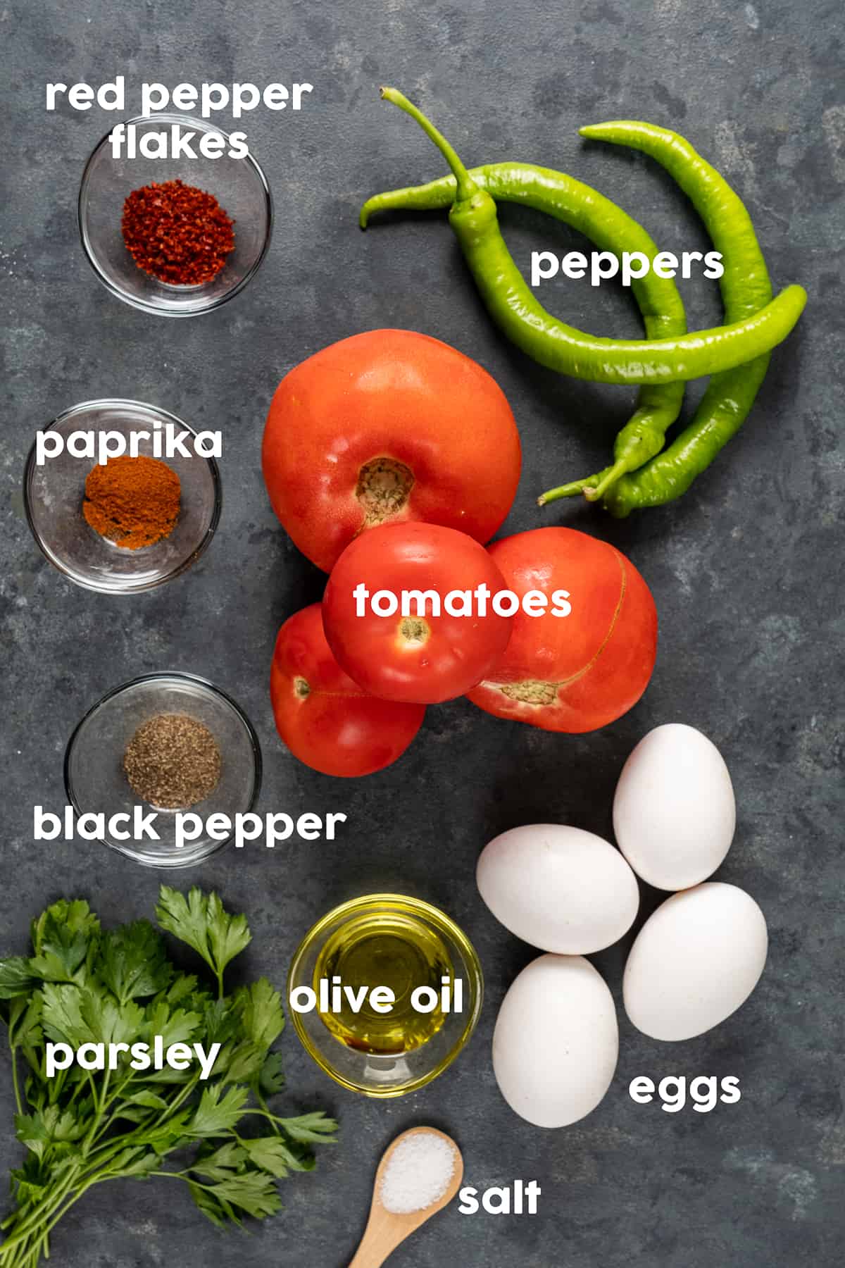 Tomatoes, Turkish green peppers, eggs with their shells, spices, parsley and olive oil on a dark background.