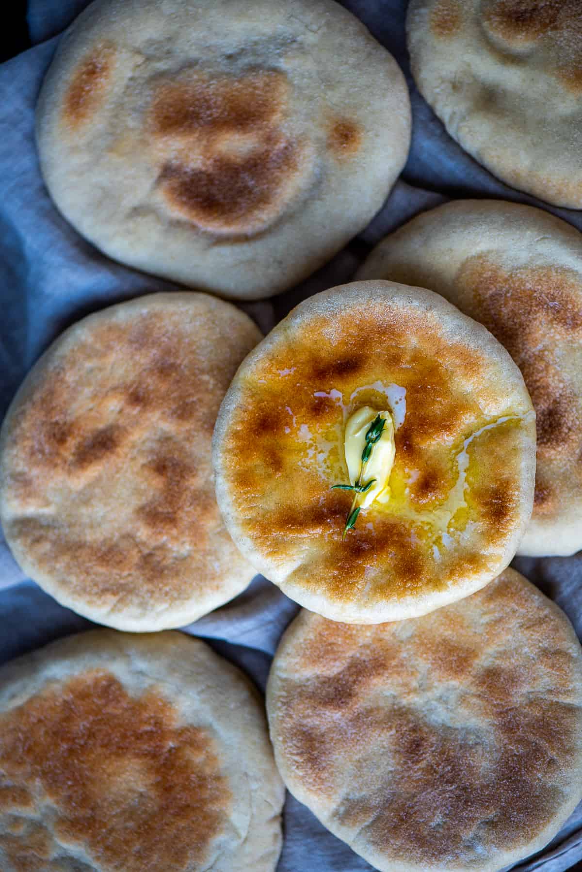 Turkish flat breads on a kitchen towel, one is topped with butter and thyme.