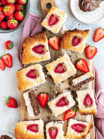 Coconut ice with a chocolaty bottom and strawberry topping sliced on a wooden board.