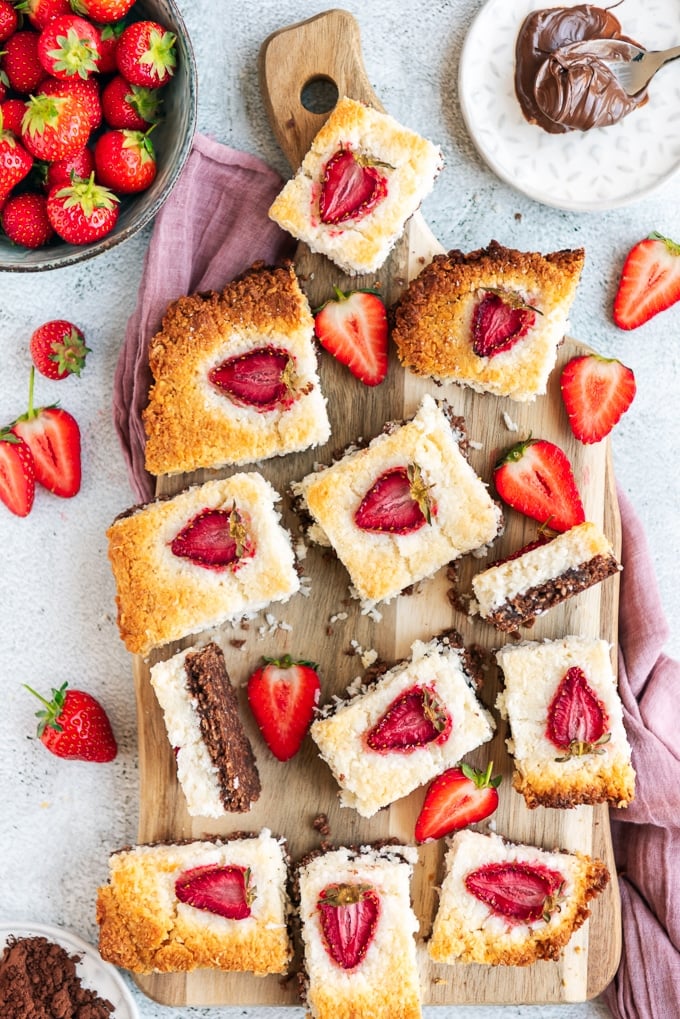 Coconut ice with strawberries and chocolate on a wooden board accompanied by fresh strawberries, cocoa powder and chocolate.