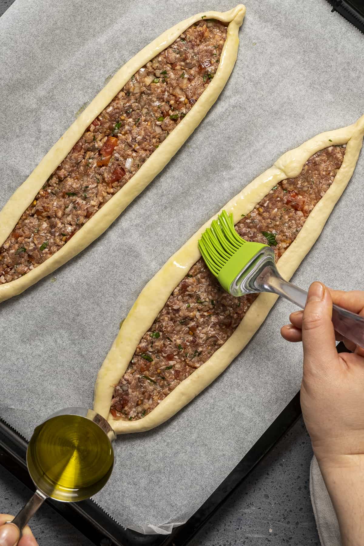 Hands brushing pide with olive oil.