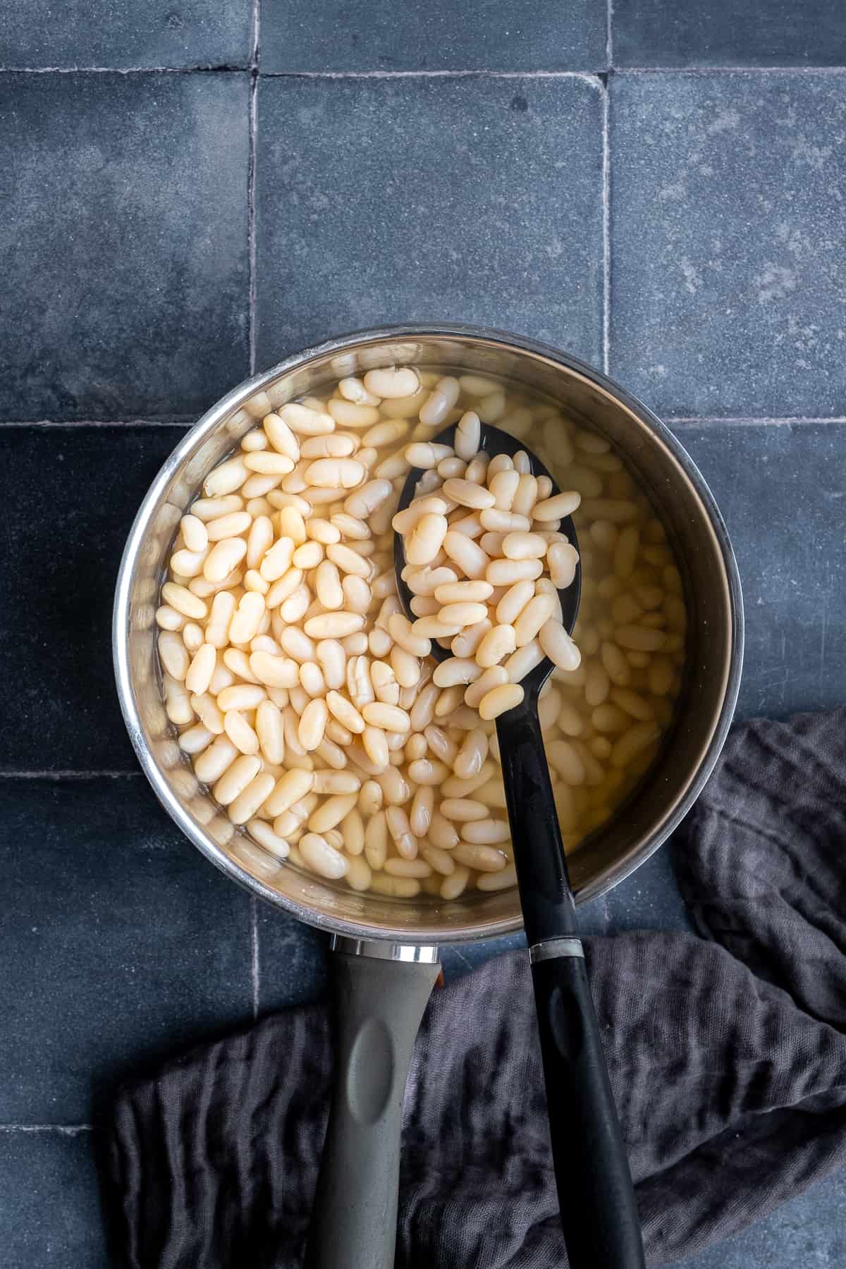 White beans boiled in a pot and a spoon inside it.