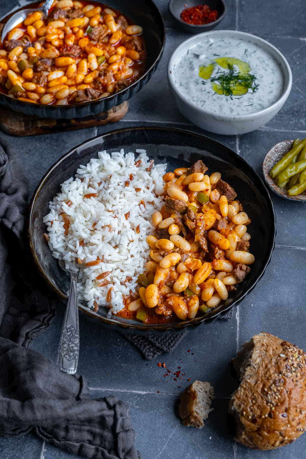 Turkish beans and rice pilav in the same bowl, cacik, pickles and another bowl of bean stew accompany.