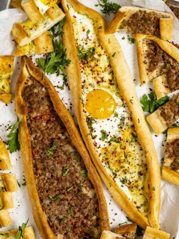 Ground meat pide and cheese pide with an egg topping in a baking tray.