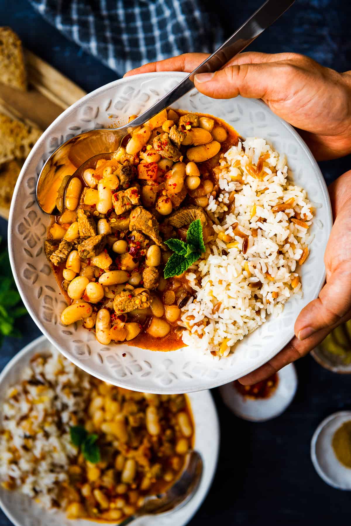 Woman hands holding a bowl filled with bean and beef stew paired with rice and orzo.