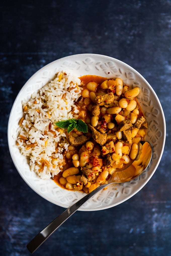 Turkish beans with lamb served in a white bowl with rice on the side.