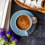Turkish coffee served in a grey coffee cup and accompanied by Turkish delights, wild flowers and newspaper on a dark background.