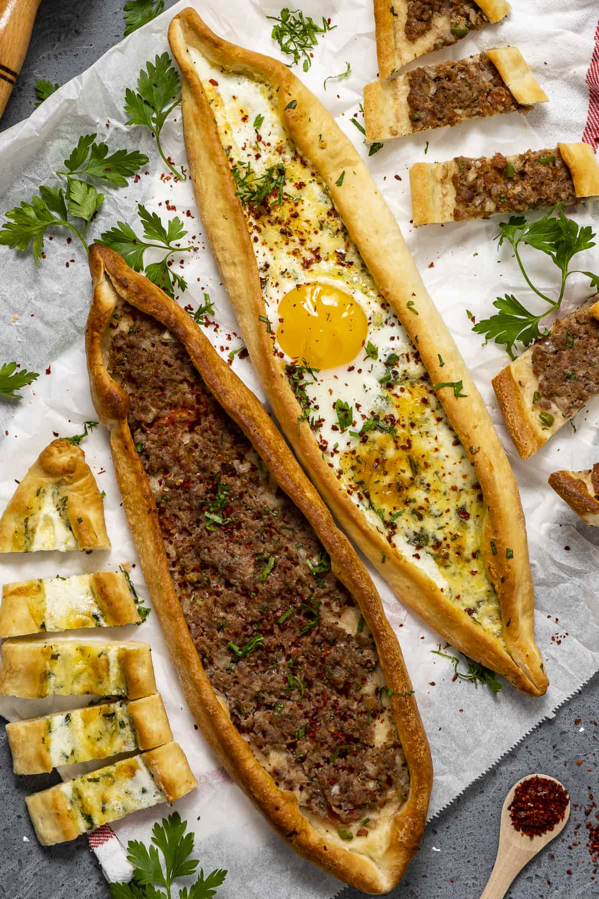 Turkish meat pide and cheese pide with an egg topping on a piece of baking paper.